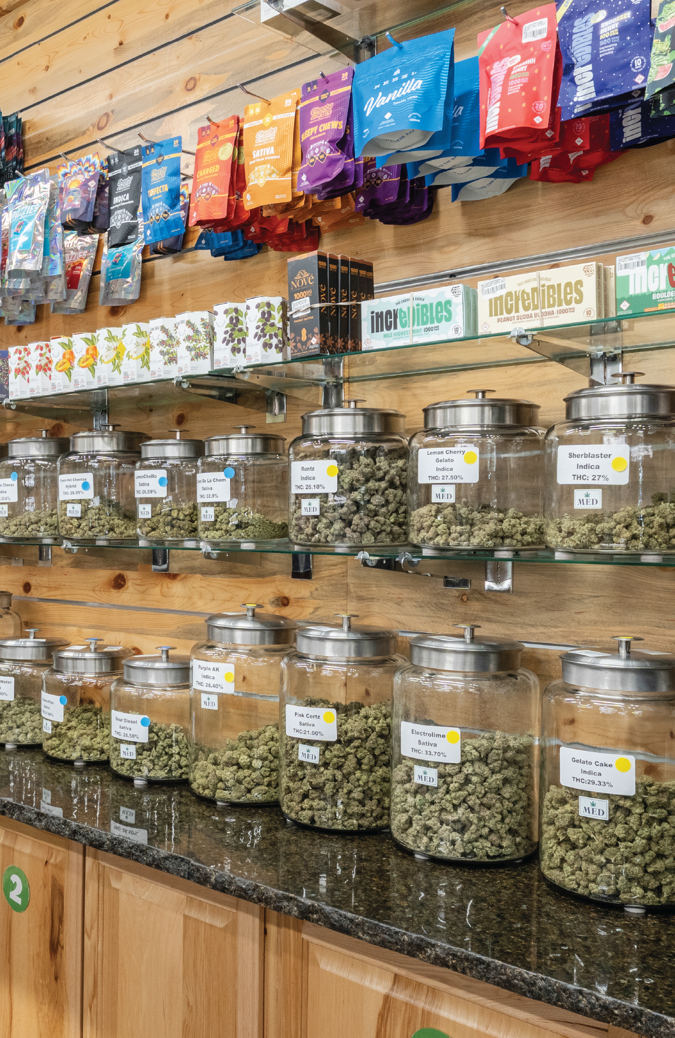 A side view of the premium selection of cannabis products at Life Flower Dispensary in Glendale, Colorado, including 14 jars of marijuana flower under an assorted collection of edibles.